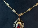 a gold necklace with a red stone on it sitting on a black hat