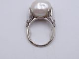 a close up of a white pearl and diamond ring on a white surface