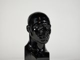 un gros plan sur une sculpture noire représentant la tête d'un homme, posée sur une surface blanche