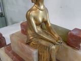une statue en or d'une femme assise sur un bloc de marbre