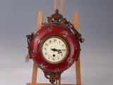 une petite horloge rouge posée sur un chevalet en bois, sur un fond gris