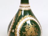 un vase vert et doré posé sur une surface blanche