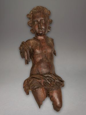 une vieille statue en bois représentant un bébé assis sur une surface blanche