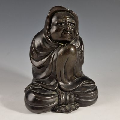 une statue antique en bronze représentant une personne assise en position de méditation