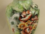 a green vase with flowers painted on it with a gold rim