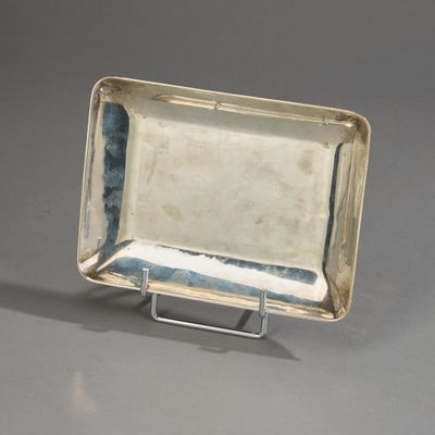 un plat ancien en argent posé sur un socle en métal, sur une surface grise