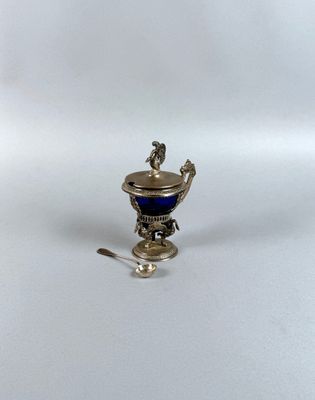 une coupe ancienne en argent et verre bleu, accompagnée d'une cuillère, posée sur une surface blanche