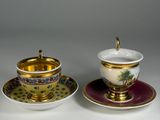 two cups and saucers with a gold rim and a purple saucer