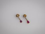 une paire de boucles d'oreilles roses et dorées posées sur un fond blanc