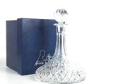 un flacon de parfum en verre posé devant une boîte bleue