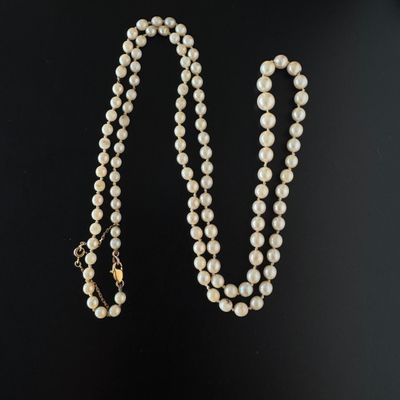 un collier de perles blanches avec un fermoir en or sur fond noir