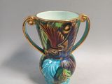 a colorful vase with a gold handle on a white surface