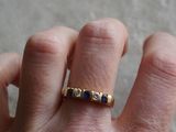 la main d'une personne portant une bague en or sertie de pierres bleues et blanches