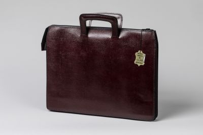 La mallette est marron et porte un emblème doré.