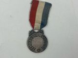 un gros plan d'une médaille posée sur une surface blanche, accompagnée d'un ruban rouge, blanc et bleu