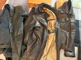 une veste en cuir noire et une veste en cuir marron posées sur un lit