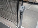 a parking meter in front of a fence in a parking lot
