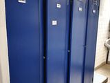 three blue lockers in a public bathroom with a urinal