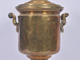 brass urn with two handles on a stand on a white background