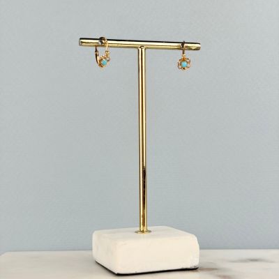 une paire de boucles d'oreilles posée sur un présentoir, sur une surface en marbre