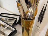 a gold vase filled with silver spoons and silverware