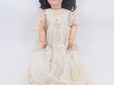 an old doll with black hair and a white dress sitting on a white surface