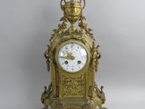 une horloge dorée posée sur une surface blanche, à côté d'une aiguille