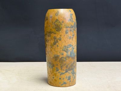 un vase jaune posé sur une table, sur fond noir