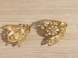pair of gold tone fish brooches on a wooden surface