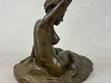 bronze statue of a woman sitting on a rock with her hands on her head