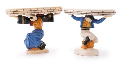 two figurines of a man carrying a basket on his head
