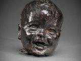 une sculpture en bronze représentant la tête d'un bébé sur une surface grise