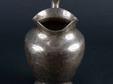 an antique silver pitcher with a handle on a black background