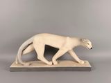 une sculpture blanche représentant un chat marchant sur un socle en bois