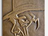 une plaque en bronze représentant un homme coiffé d'un chapeau et portant une moustache