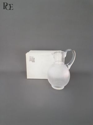 La cruche blanche se trouve à côté de la boîte, sur la table.