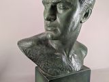 statue of a man ' s head on a pedestal with a vase in the background