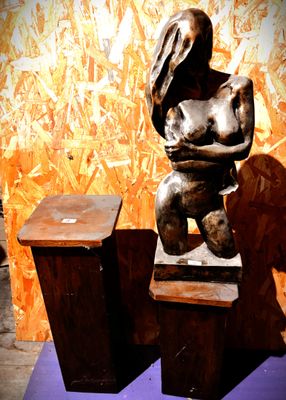une statue représentant une femme assise sur deux tabourets en bois
