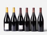 six bottles of wine lined up in a row on a white surface
