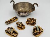 une image représentant un bol en argent et six petites figurines posées sur une surface blanche