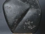 a black stone sculpture on a wooden stand against a gray background
