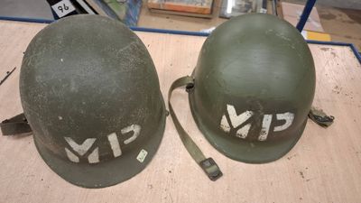 pair of army green helmets with white letters on them sitting on a table