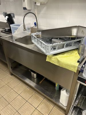 un évier en acier inoxydable dans une cuisine professionnelle, avec une serviette jaune posée sur le plan de travail