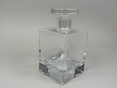 flacon de parfum en verre transparent avec un bouchon argenté, posé sur une surface blanche