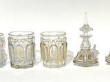 cinq vases en verre et un bougeoir posés sur une surface blanche