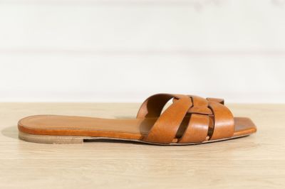 un gros plan sur une paire de sandales marron posées sur une surface en bois