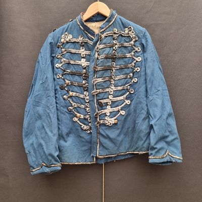 Une vieille veste bleue à boutons argentés est suspendue à un cintre en bois.