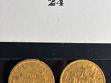 two gold coins are sitting on a black surface next to a white box