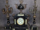 une horloge noire posée sur une table, à côté d'un bouquet de bougies