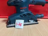 une ponceuse orbitale Bosch posée sur une table, à côté d'une boîte rouge